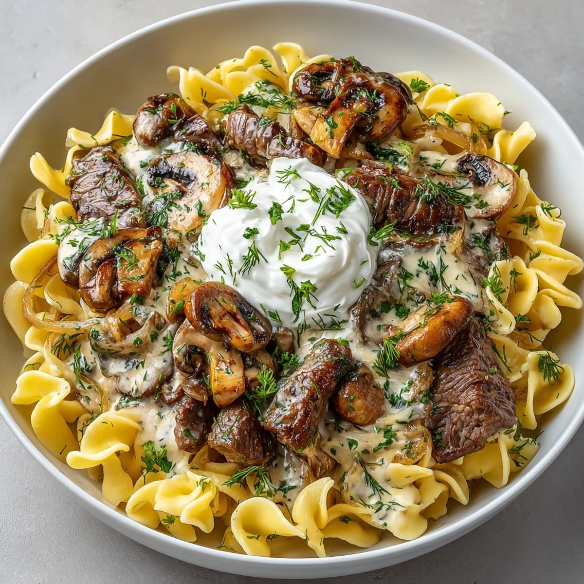 Classic Beef and Mushroom Stroganoff served over buttery egg noodles, topped with fresh parsley and dill.
