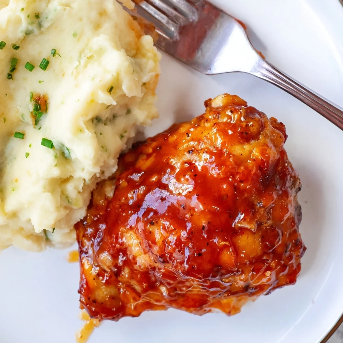 Oven-baked honey BBQ chicken thighs glisten next to fluffy garlic mashed potatoes.  
