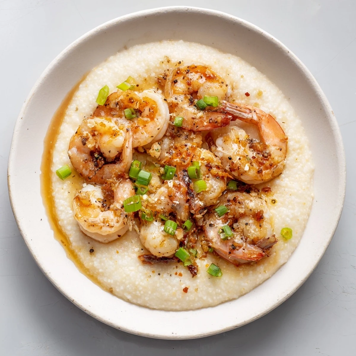 A close-up of steaming Shrimp & Grits: plump shrimp over rich grits, garnished with green scallions.