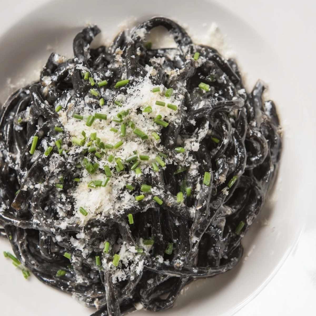 Silky Squid Ink Pasta with creamy sauce, Parmesan, and chives, ready to serve and enjoy.
