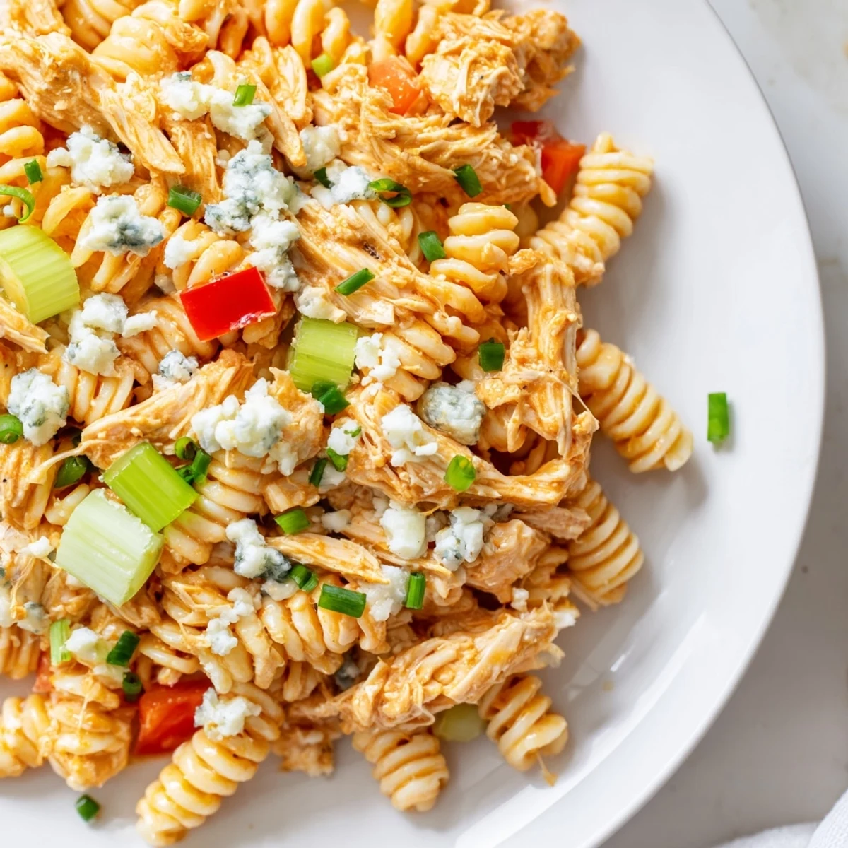 Buffalo Chicken Pasta Salad served in a rustic white bowl, garnished with crumbled blue cheese and fresh chives on a wooden table.
