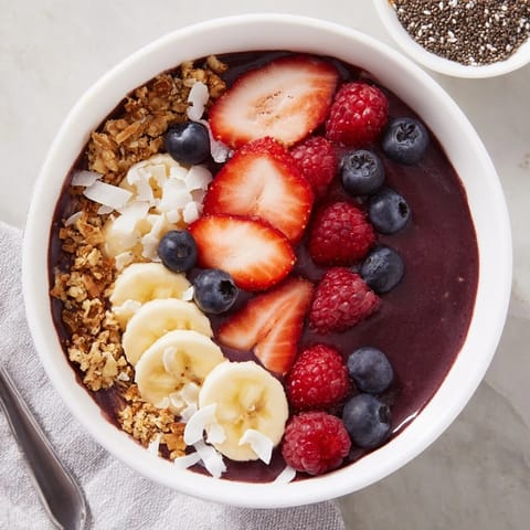 Thick and creamy acai berry smoothie bowl in a ceramic bowl, drizzled with almond butter and loaded with fresh strawberries, blueberries, and pumpkin seeds.