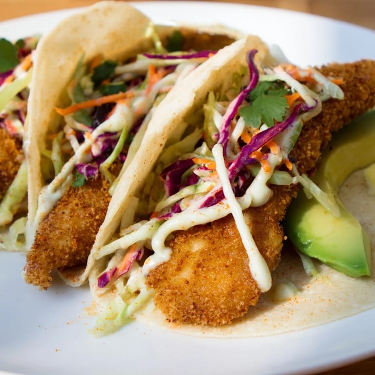 Close-up of freshly made Crispy Fish Tacos, featuring golden fish, creamy sauce, and colorful slaw.